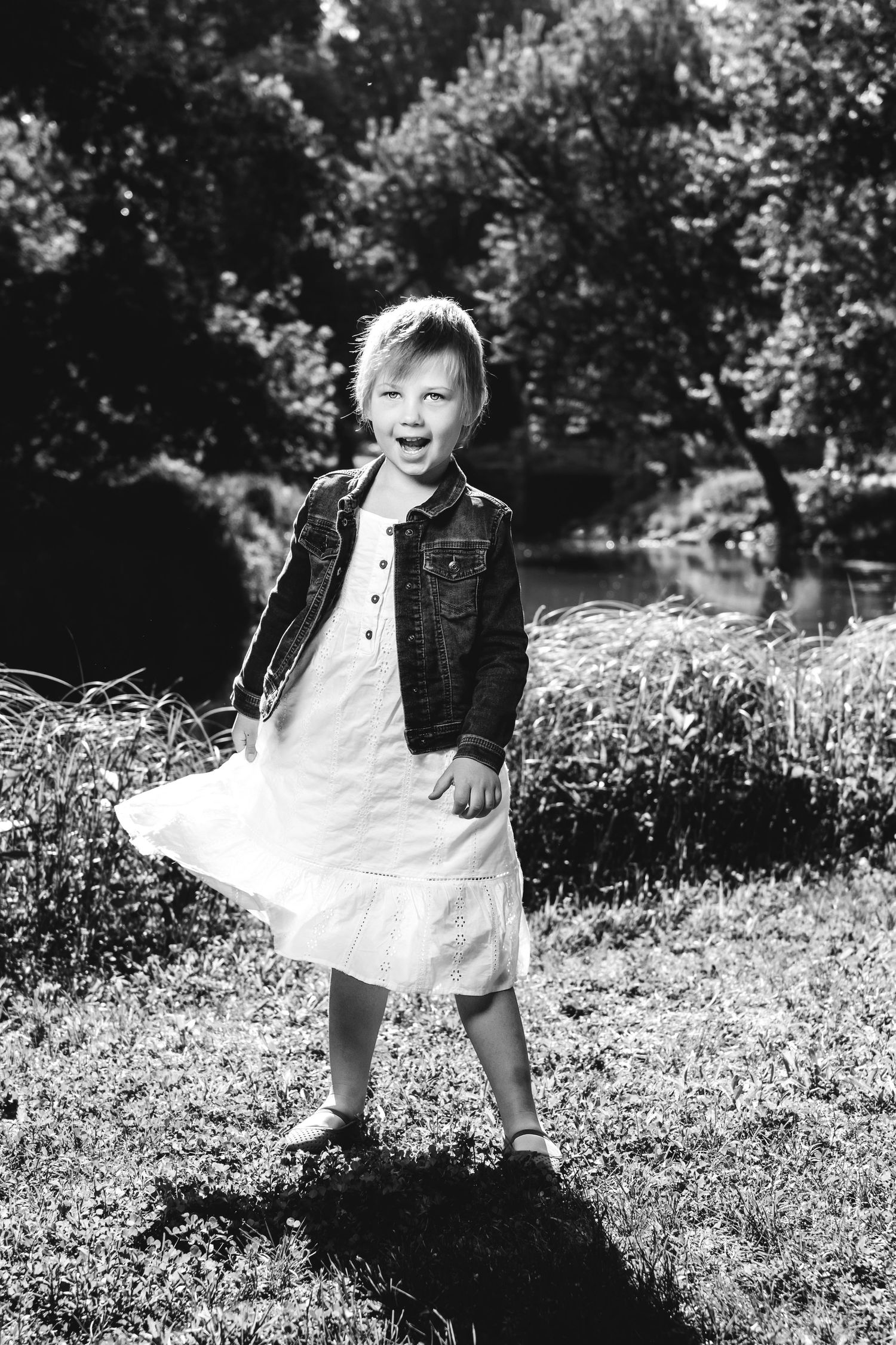 Black and white image of a young child in white dress playing joyfully in a grassy field.