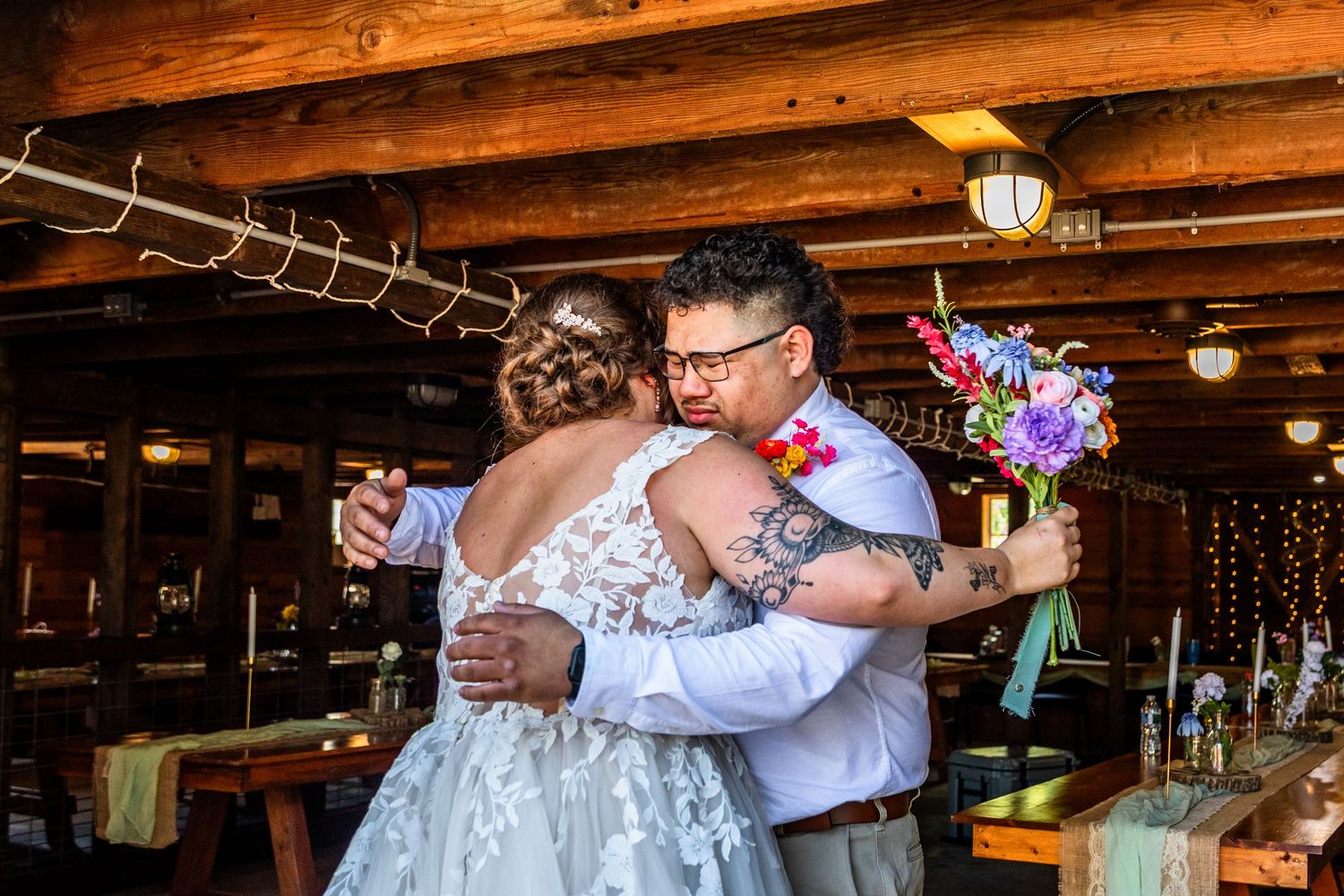 Couples dancing and celebrating at a rustic barn wedding reception with wooden beam ceiling.