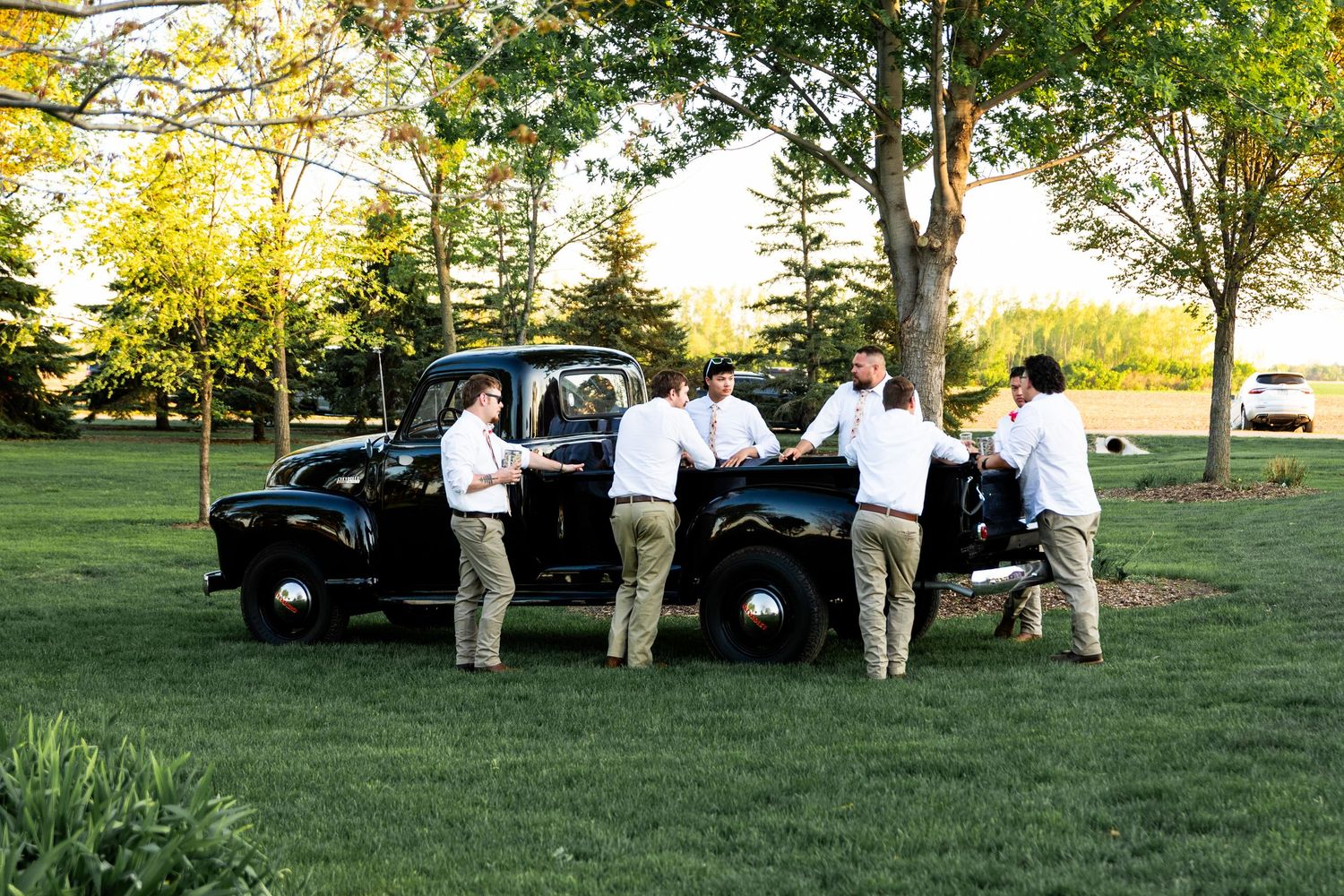 Wedding guests gather on a grassy lawn during golden hour for outdoor celebrations.