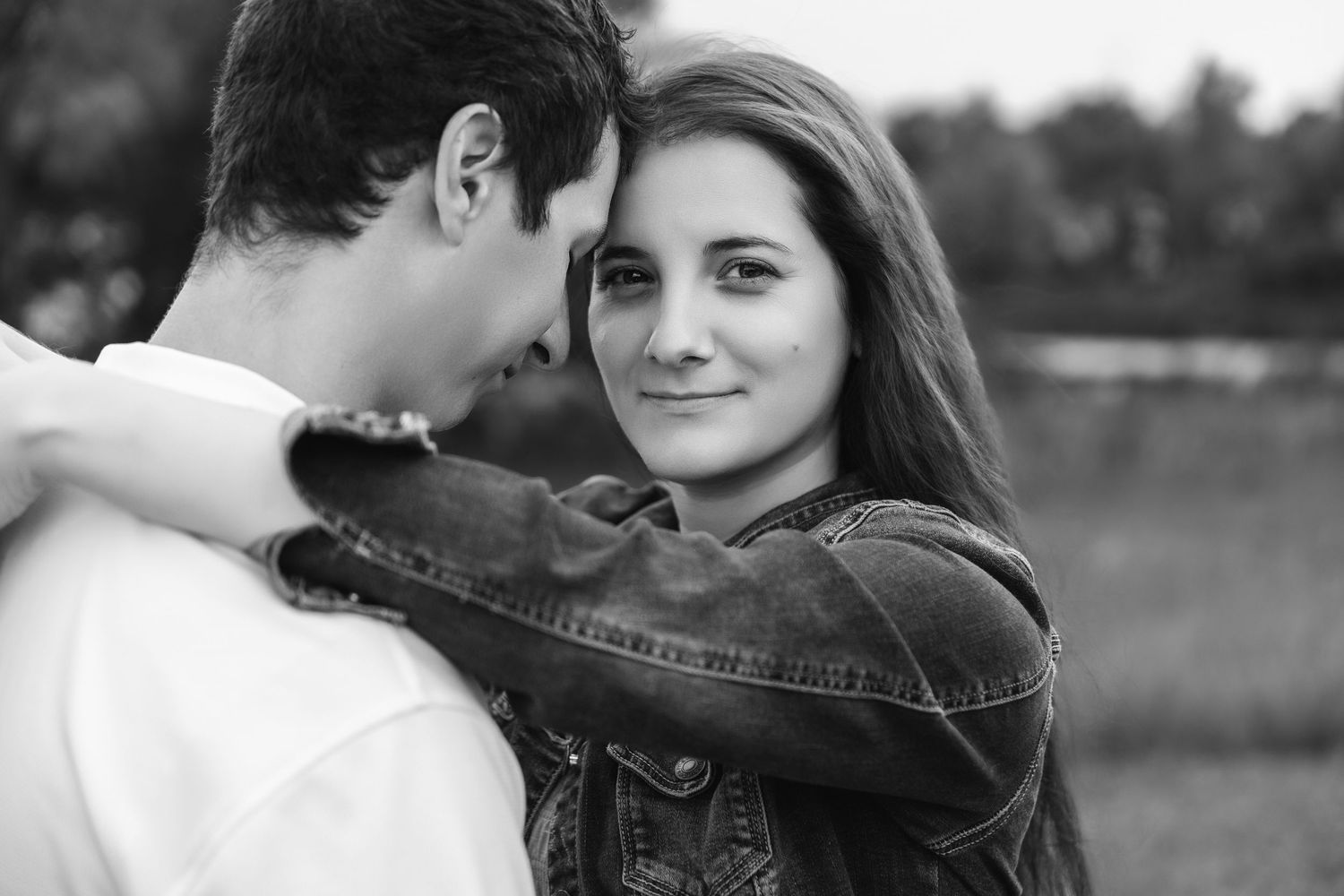 A couple shares an intimate moment in black and white photography by a lake.