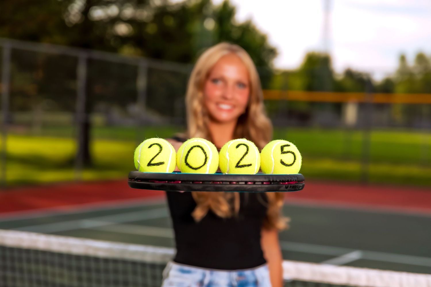 Tennis court with bright yellow tennis balls and black net in golden evening light.