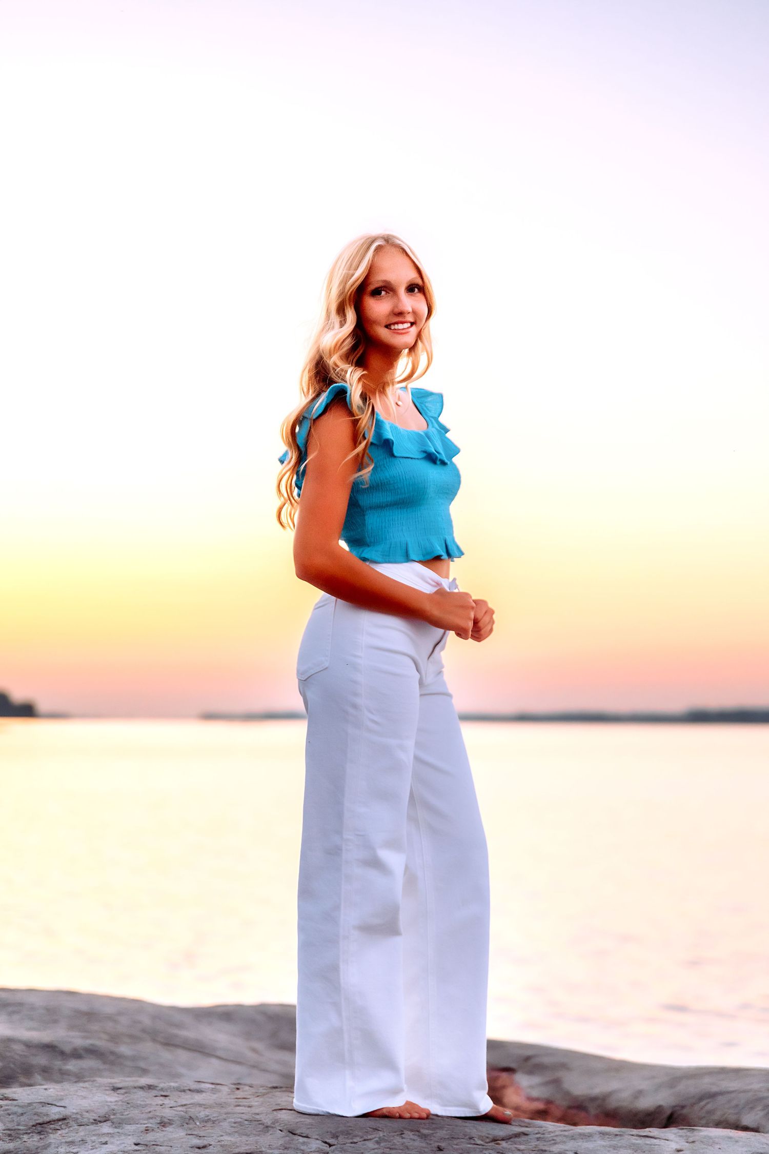 Beachside portrait series in a white skirt and blue ruffle top against a sunset sky.