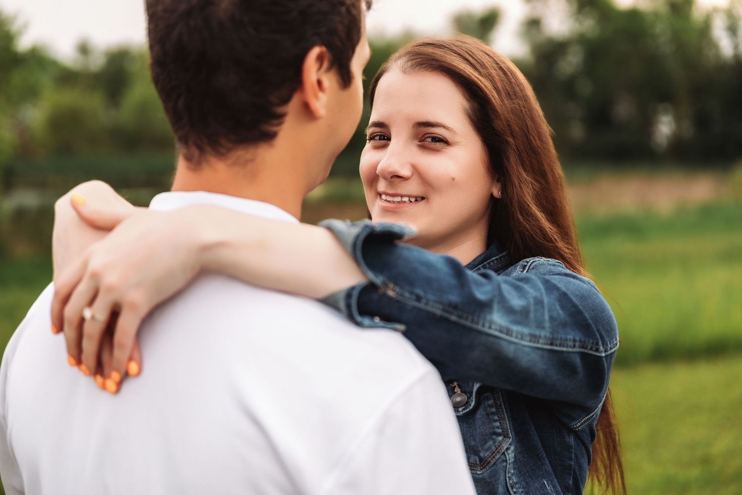 Romantic couple embraces outdoors in a green field during golden hour.