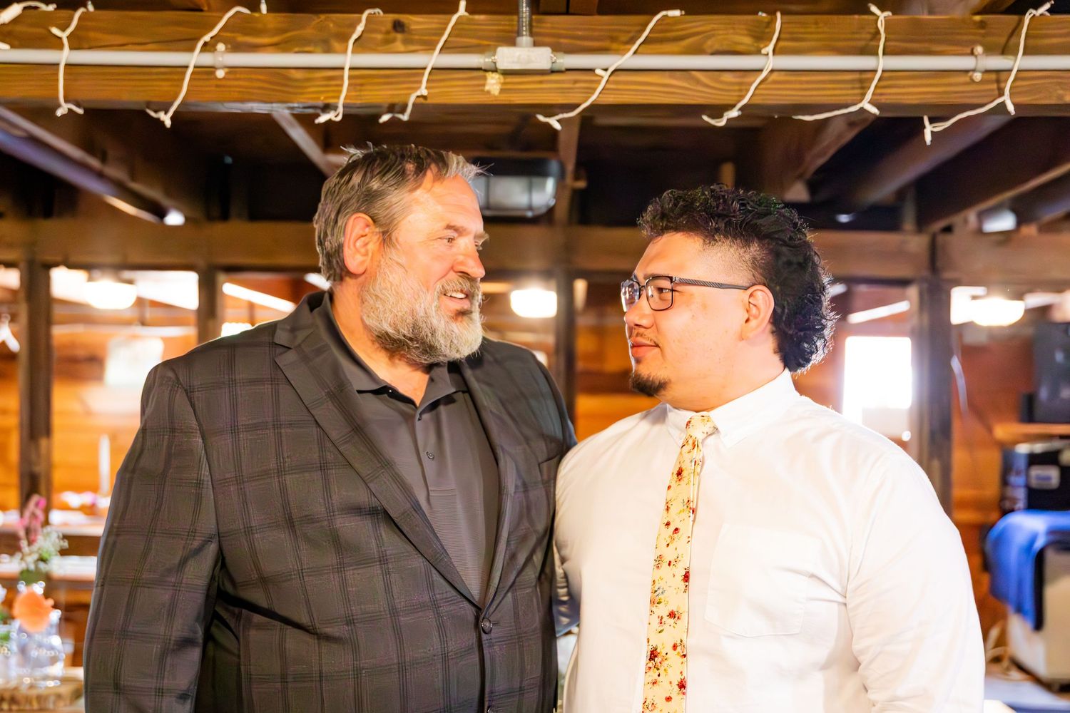 Wedding party members in white shirts and dark suits gathered in a rustic indoor venue.