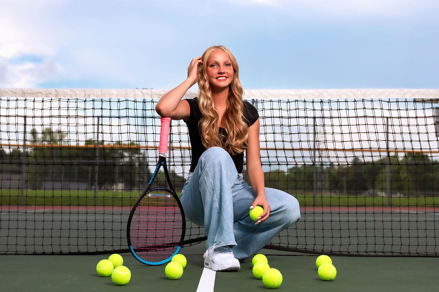 Tennis player sits on court with yellow balls scattered around and net in background at sunset.