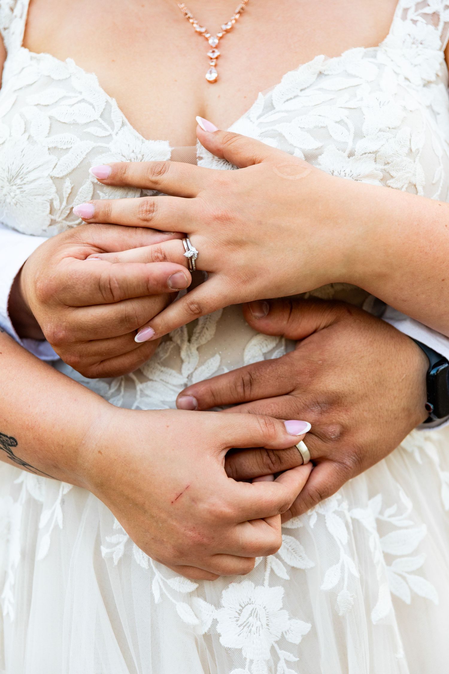 Close up of hands with wedding rings embracing over a detailed white lace wedding dress.