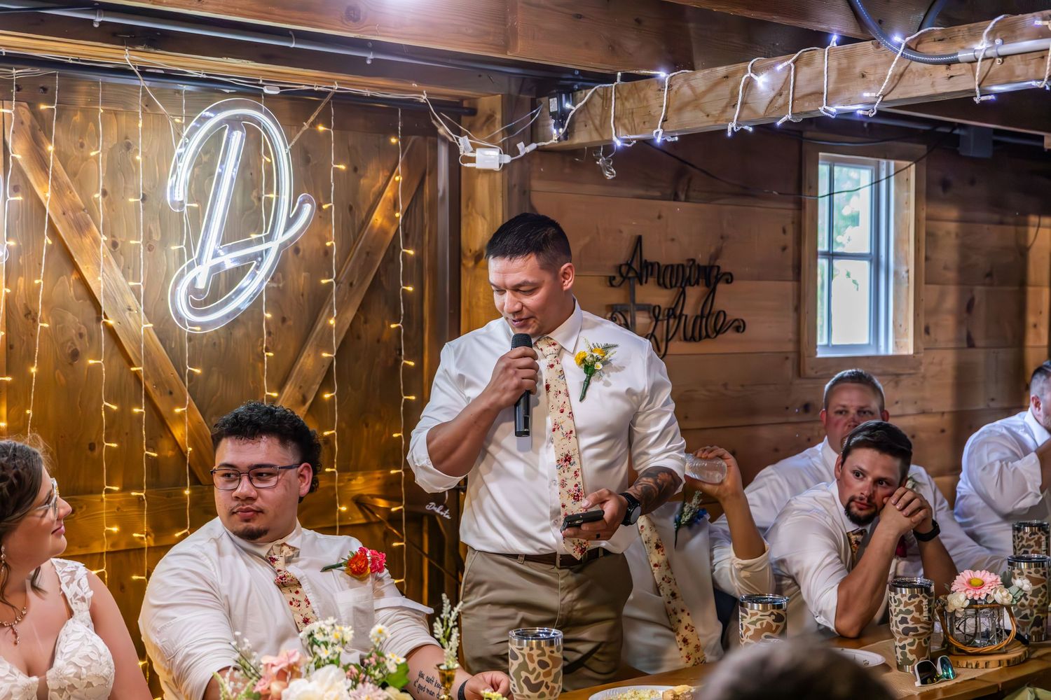 Wedding reception celebration in a wooden barn with decorative lights and table settings.
