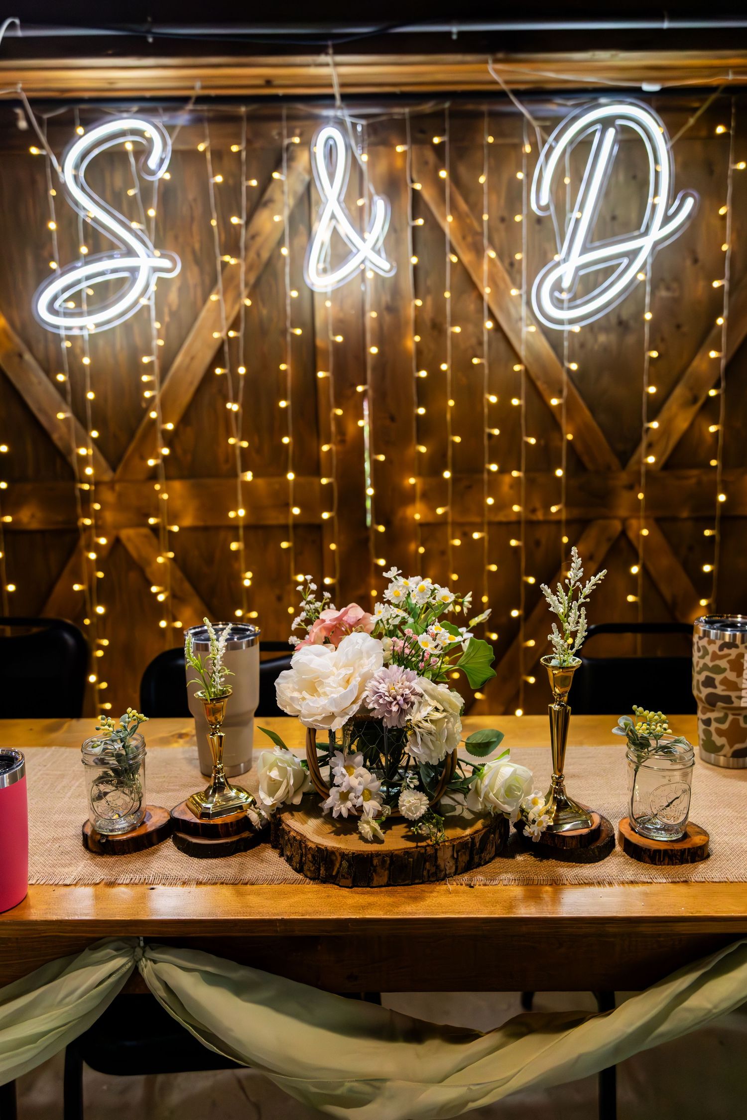 Glass bell jar terrariums with delicate floral arrangements sit beneath glowing string lights at a rustic wedding reception.