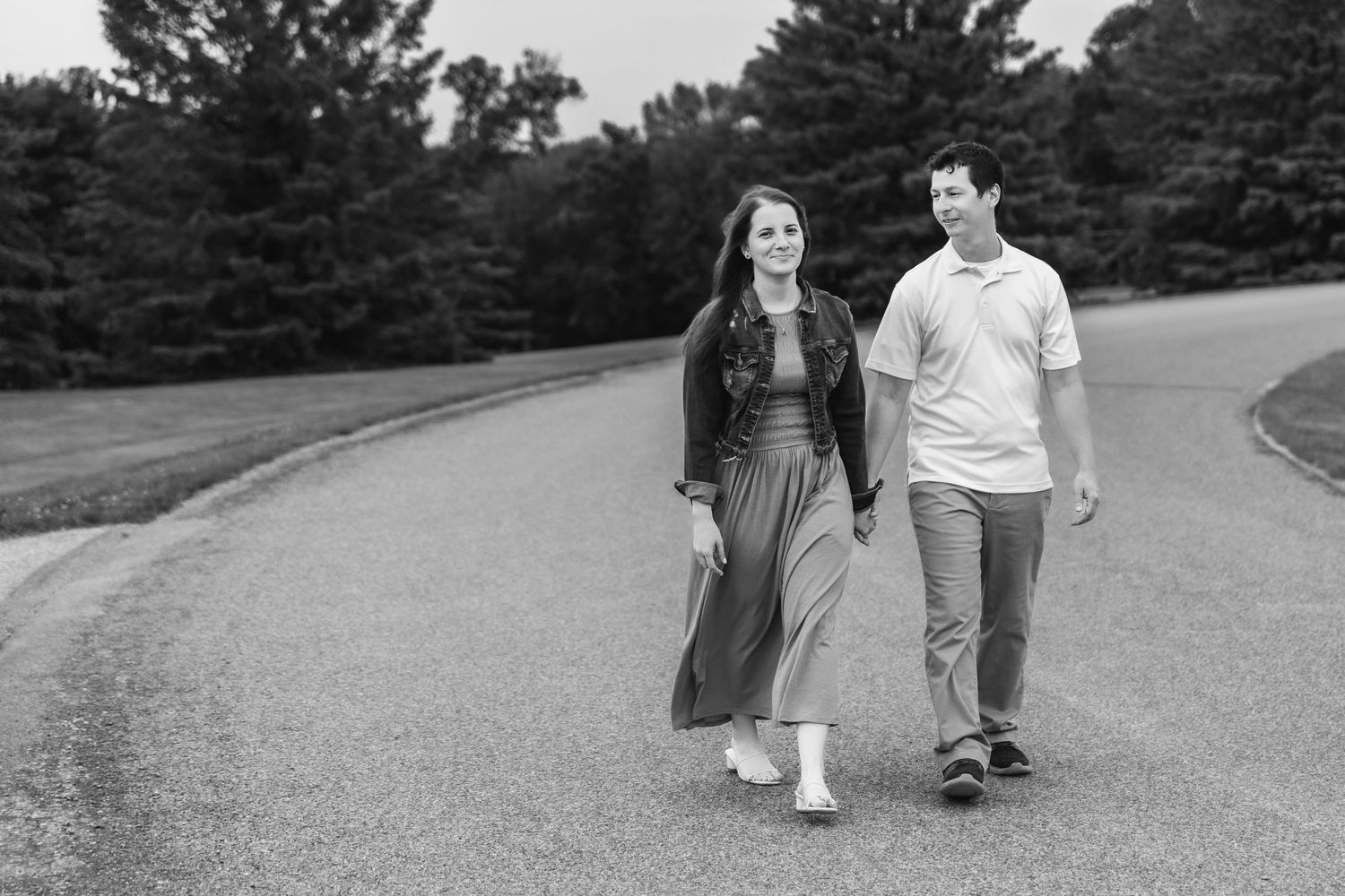 A couple walks hand in hand along a winding path outdoors in black and white photography.