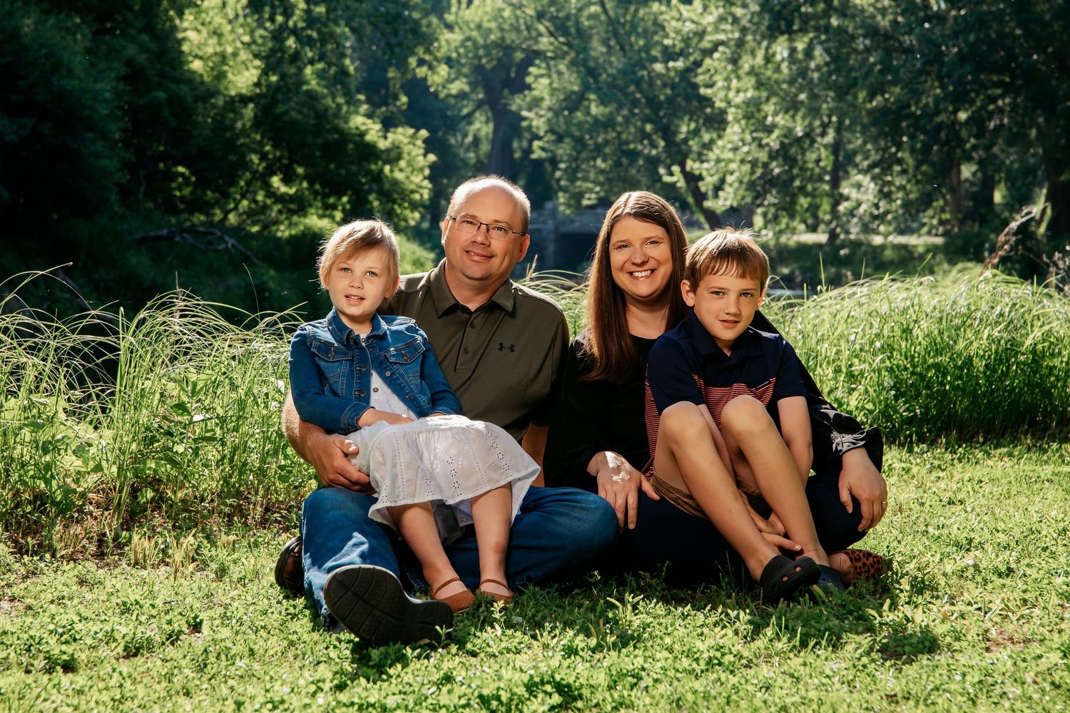 A group poses together outdoors on grass with lush greenery and trees in the background.