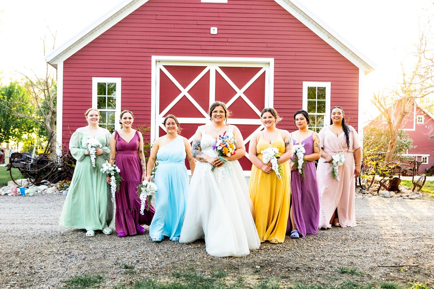 Wedding party posed in front of a classic red barn with colorful attire.