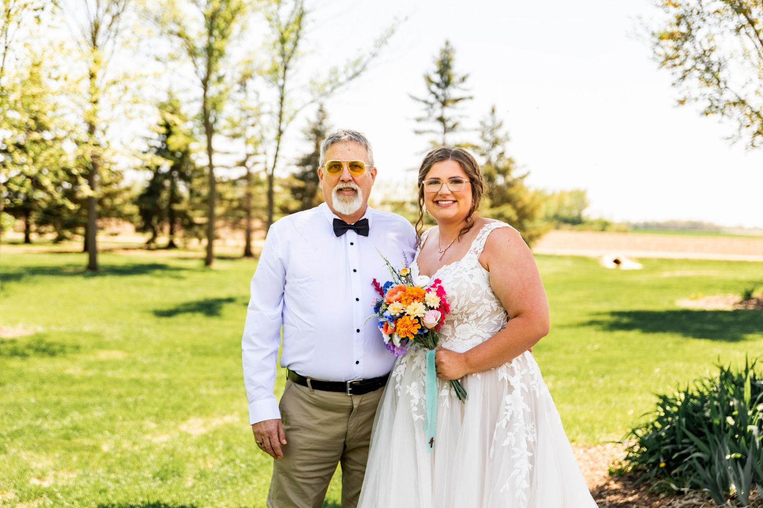 A colorful wedding party poses outdoors on a sunny day in a park setting.