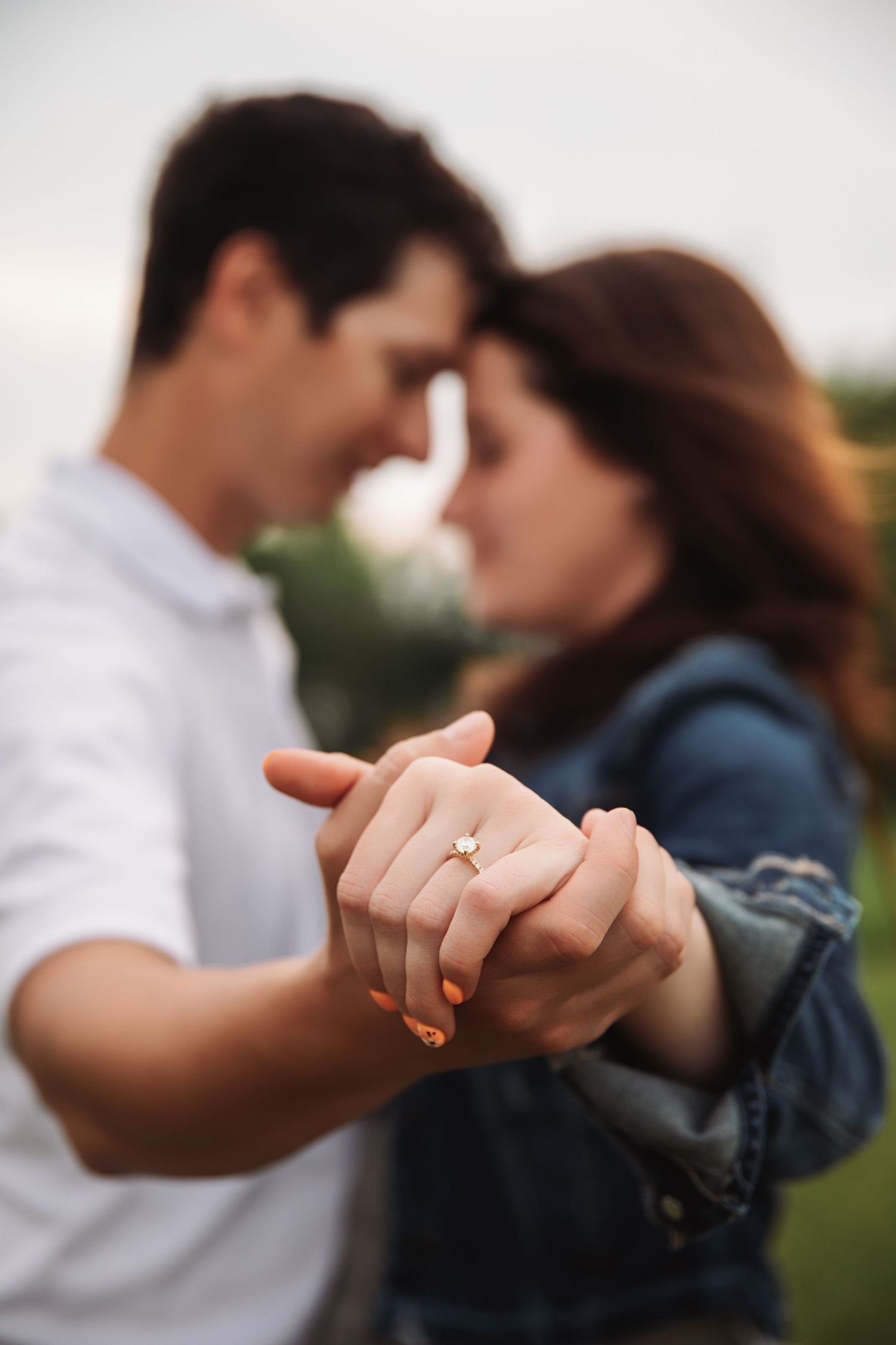 A romantic couple holds hands while dancing intimately outdoors, with a diamond engagement ring visible.