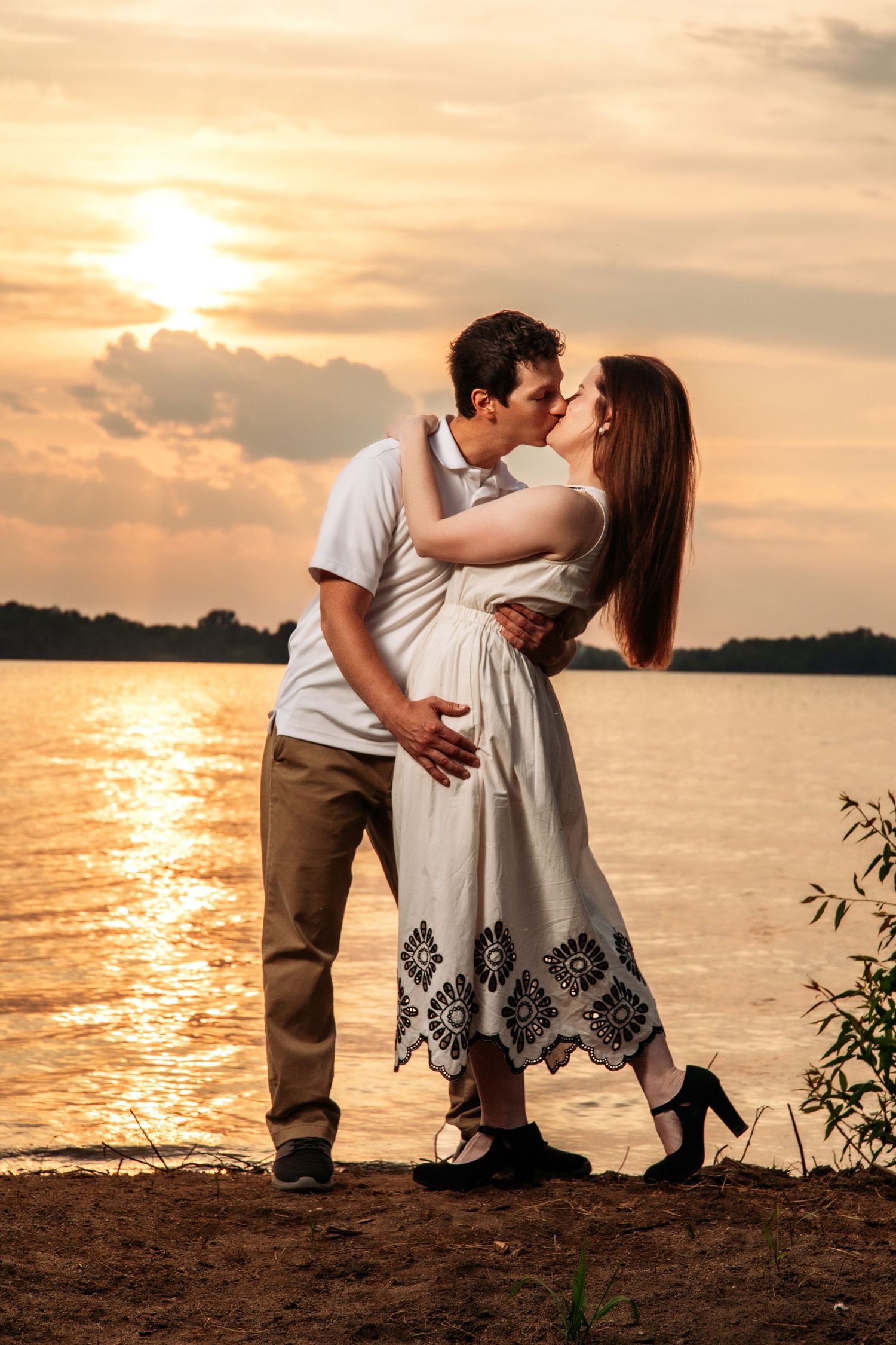 A couple embraces by the water's edge during a dramatic golden sunset.