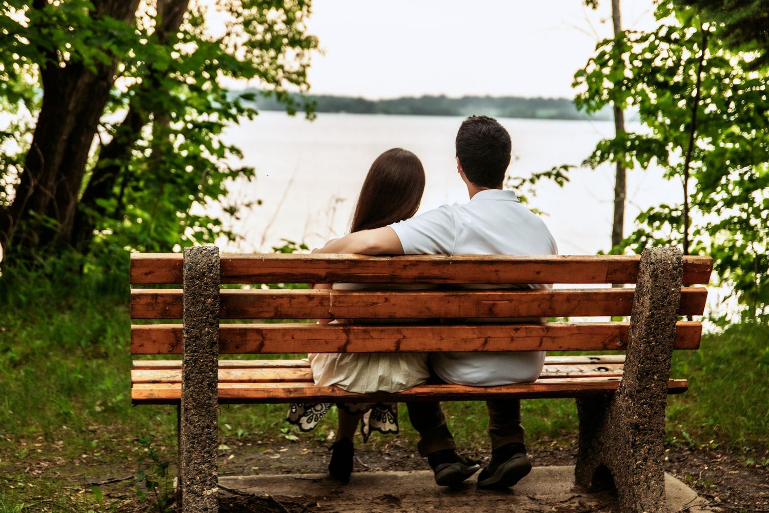 Couple sitting together on a wooden park bench overlooking a serene lake.
