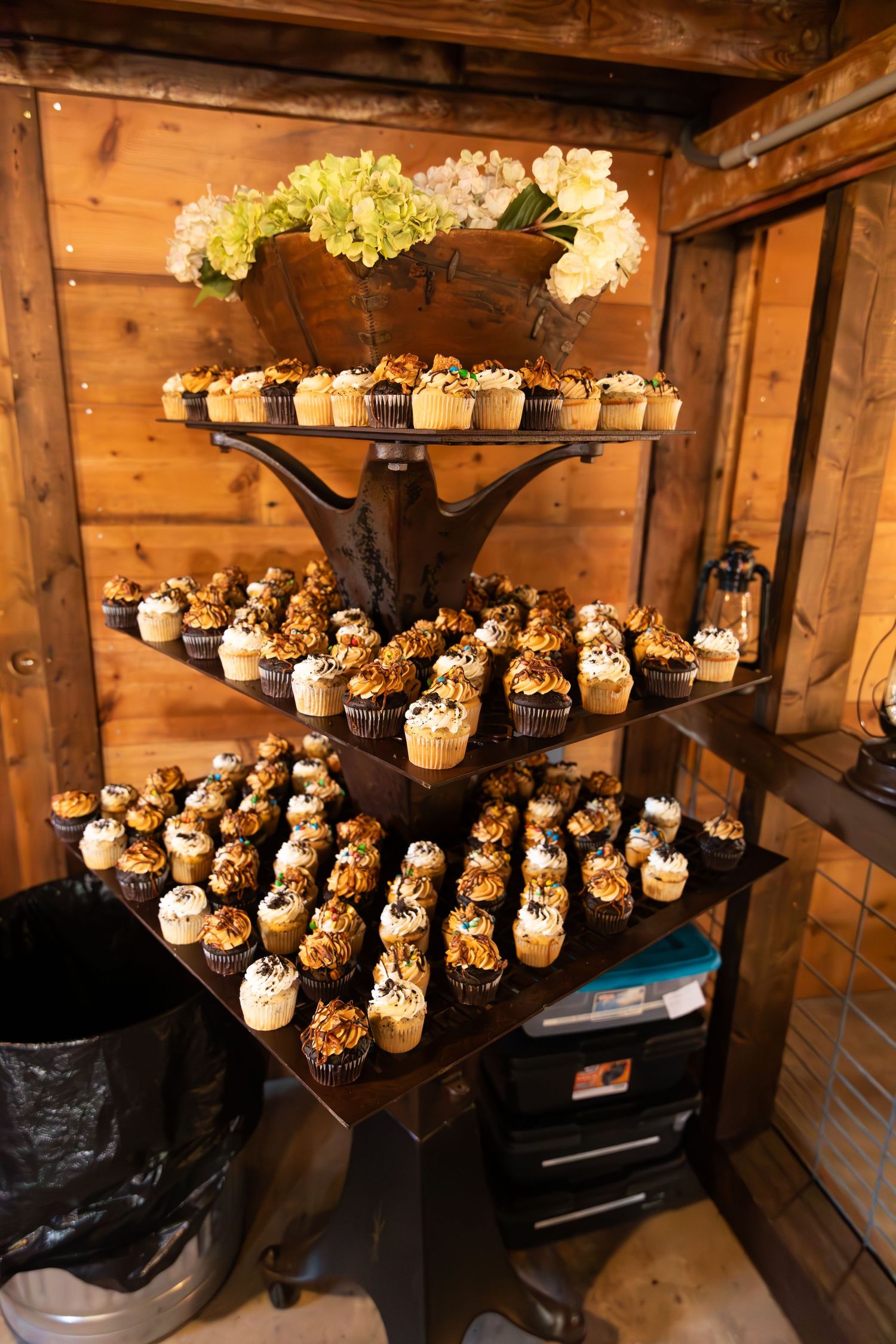 Elegant cupcake display with multiple tiers arranged on wooden shelves in a rustic barn setting.