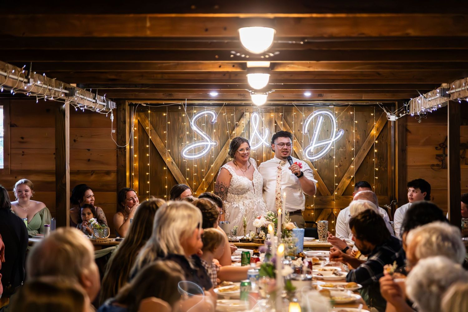 Rustic barn reception venue with exposed wooden beams and illuminated string light decorations.