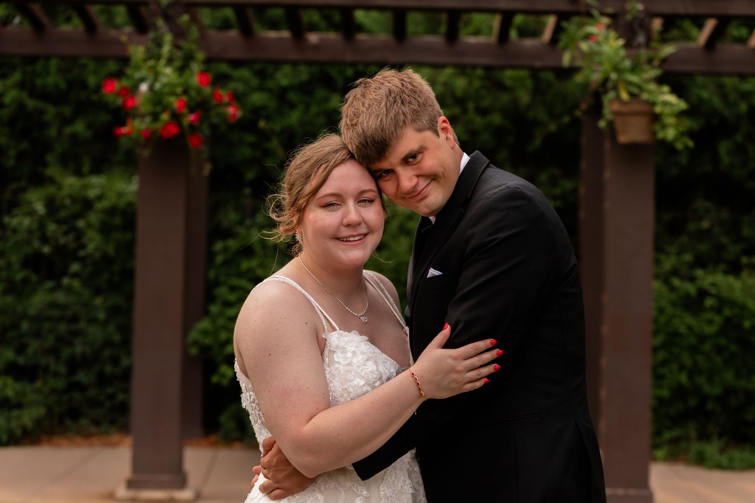 An affectionate moment between a couple in formal attire under a garden pergola with lush greenery in Sioux Falls, South Dakota.