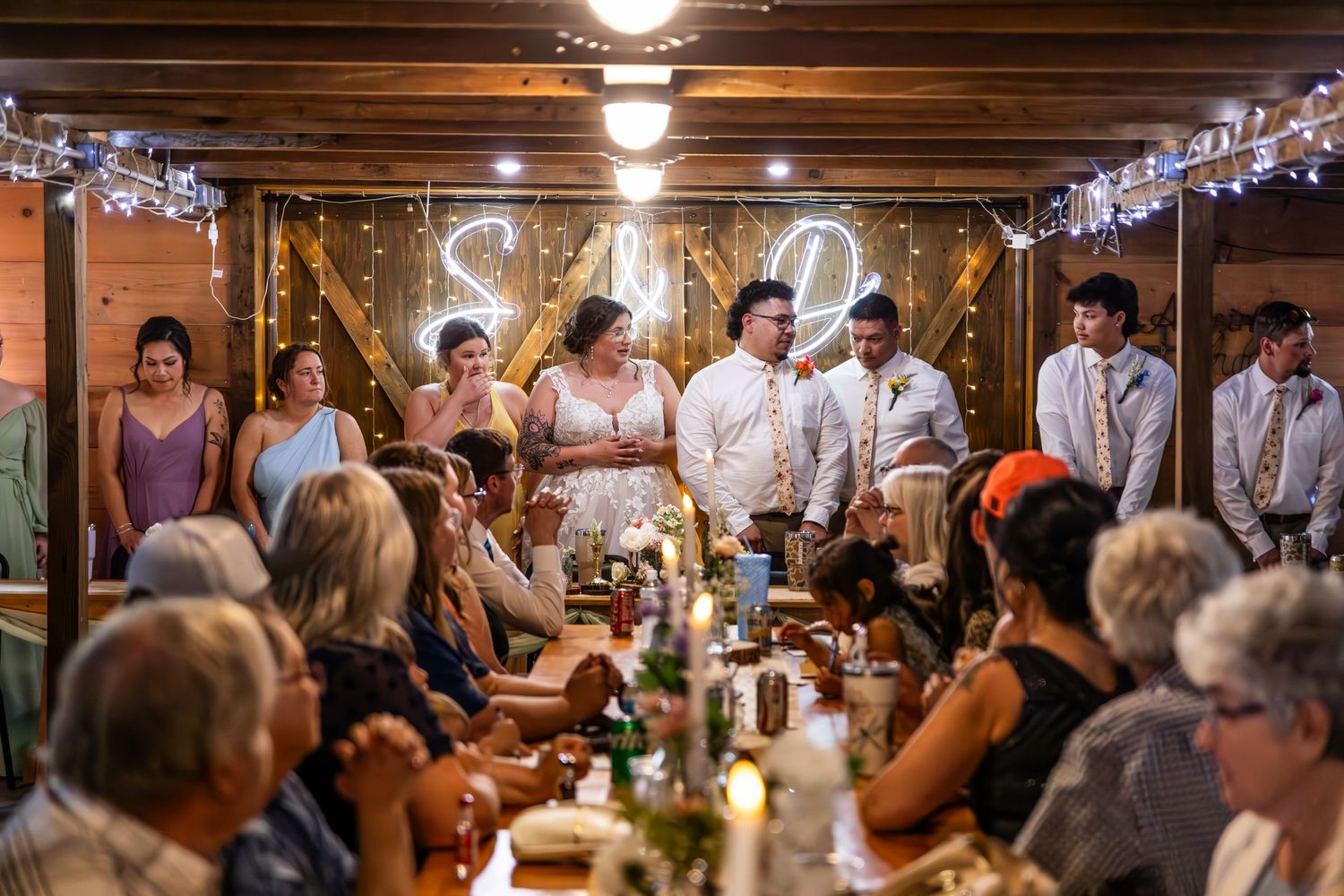 Wedding reception dinner in a rustic barn venue with string lights and long tables.