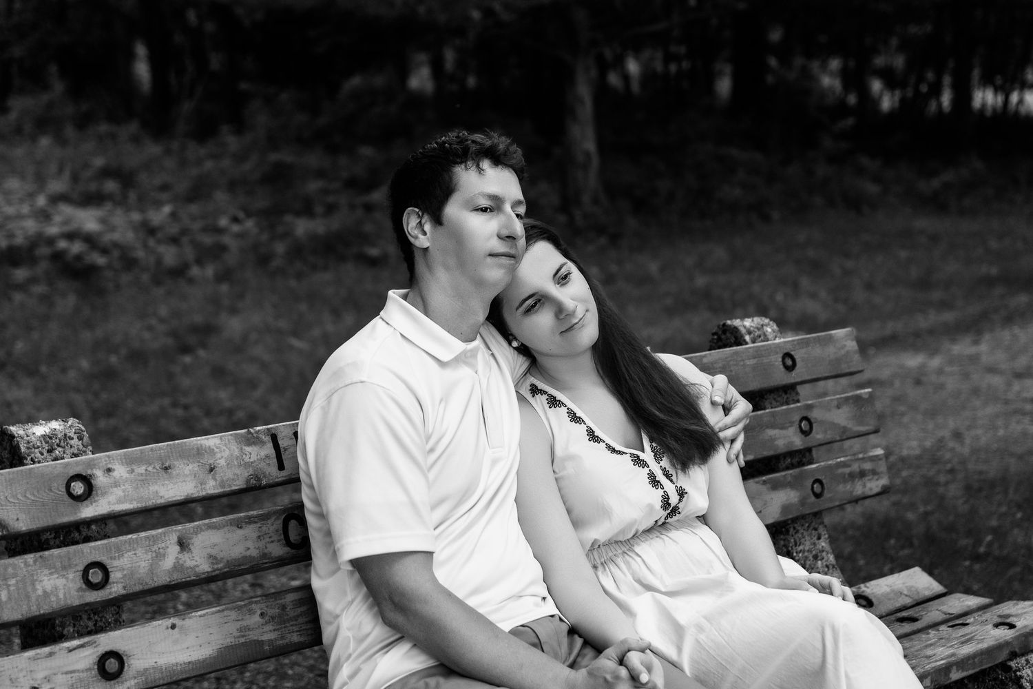 A romantic couple rests together on a wooden park bench in black and white.