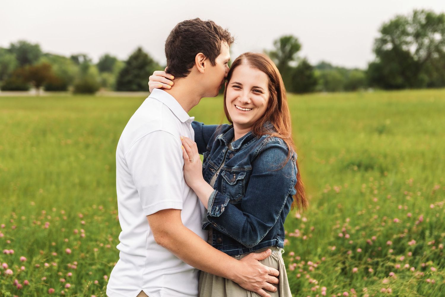 A couple embraces lovingly in a sunny meadow filled with wildflowers on a warm summer day.