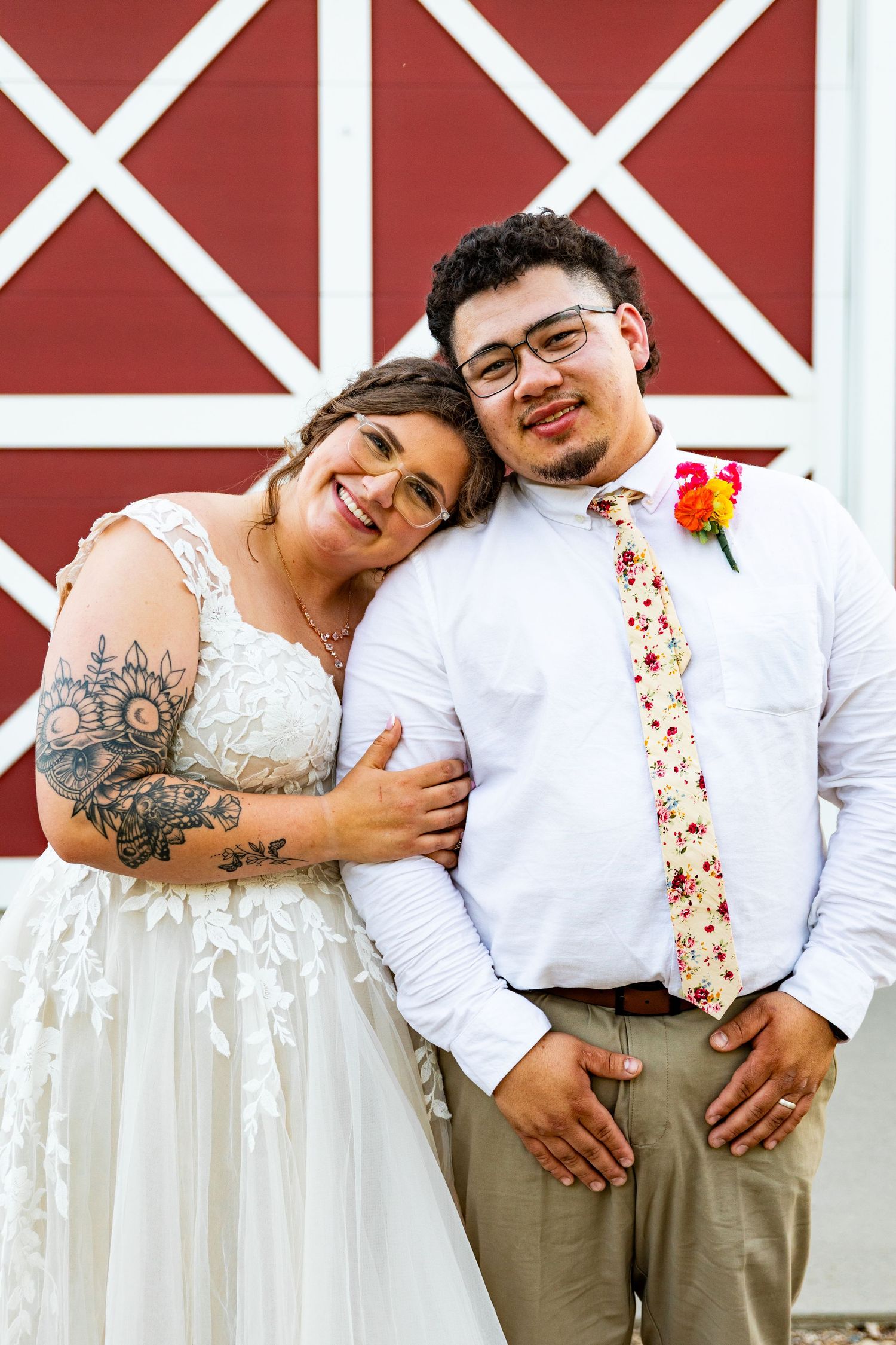 A happy couple in wedding attire pose together against a red barn backdrop.