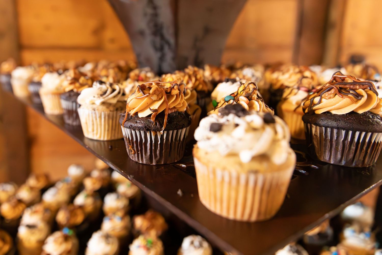 Rows of chocolate and vanilla cupcakes topped with swirled frosting and chocolate drizzle on elegant dessert displays.