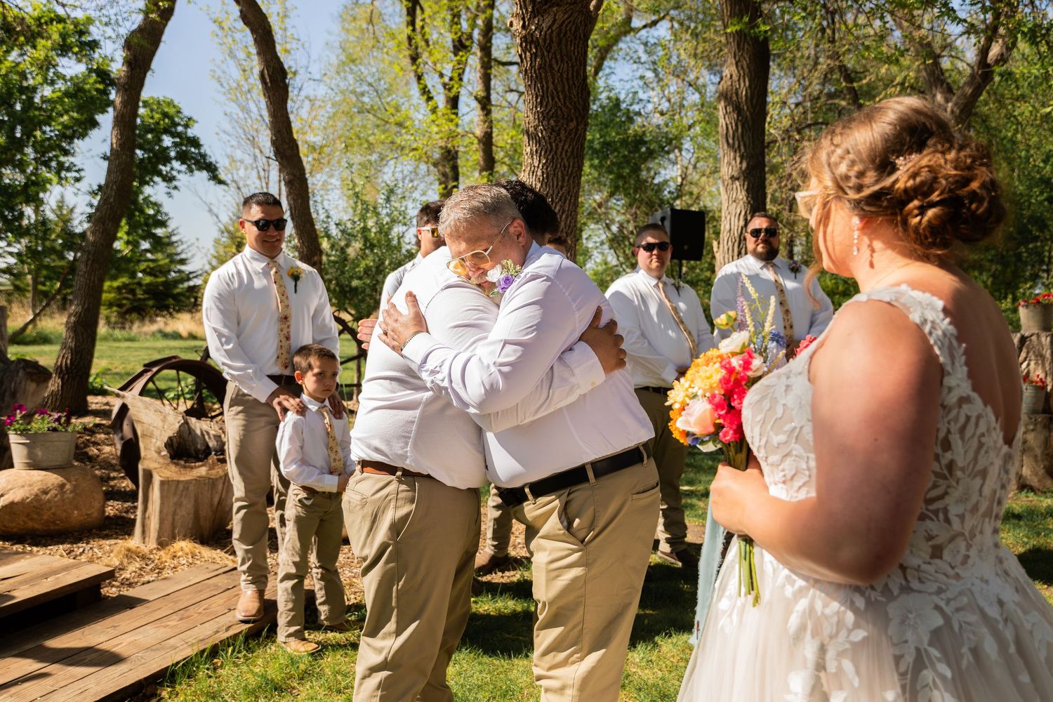 Wedding party celebrates outdoors in sunlit wooded area during emotional ceremony.