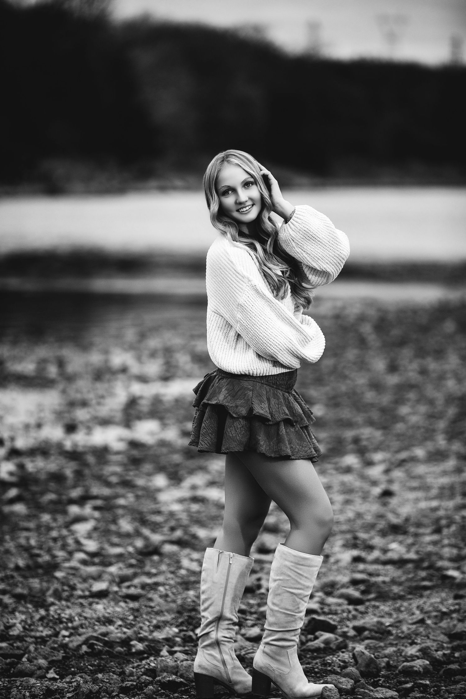 Black and white portrait with sweater and knee-high boots in natural outdoor setting.