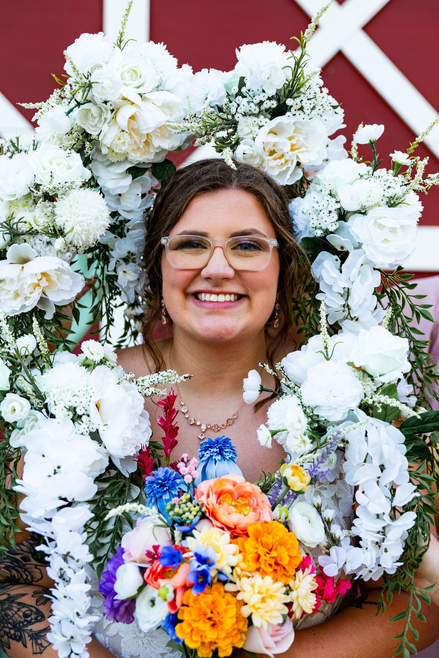 Bridal portrait surrounded by white floral arrangements and colorful bouquet against red background.