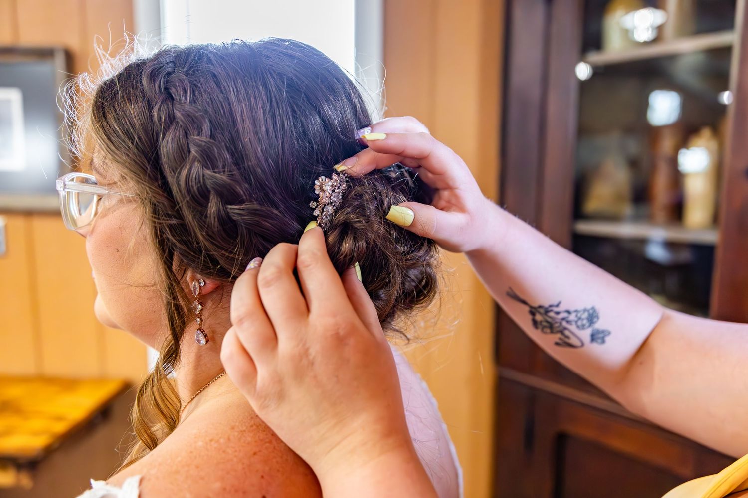 Close-up shot of hands styling an intricate braided updo hairstyle with decorative accessories.