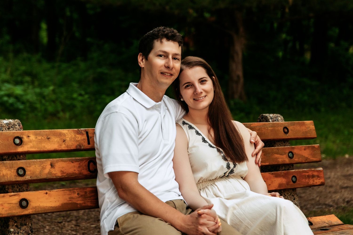 A couple sits close together on a wooden bench in a green park setting.