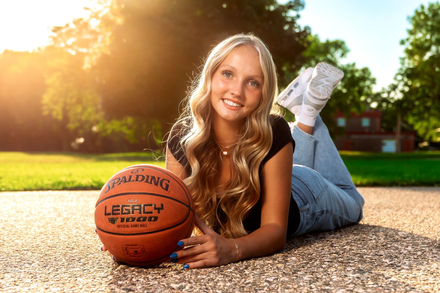 Student athlete poses with basketball on outdoor court during golden hour sunset.