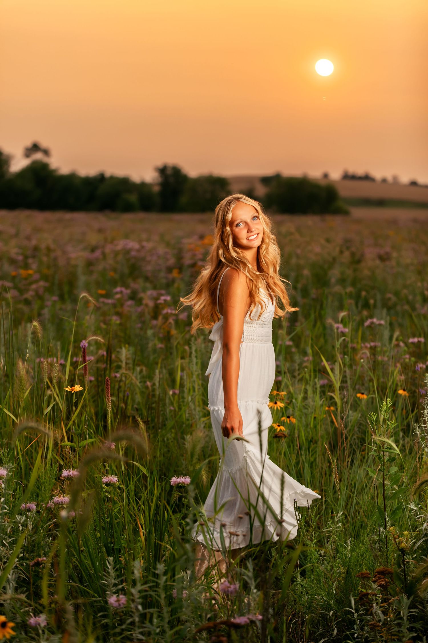 A dreamy sunset portrait in a field of wildflowers with a flowing white dress catching the evening light.