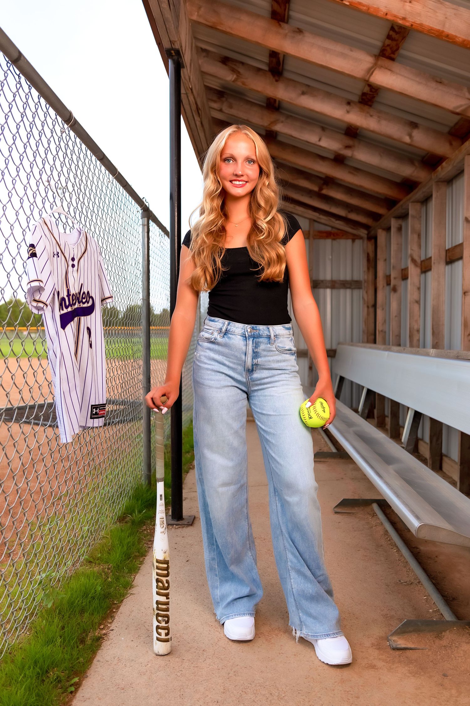 Casual sporty poses in a covered dugout area with tennis gear and light wash denim jeans.