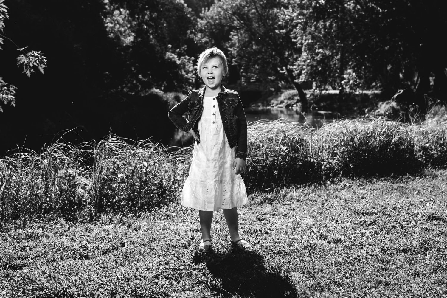 A black and white photograph of a figure standing in a grassy field wearing an apron and light colored clothing.