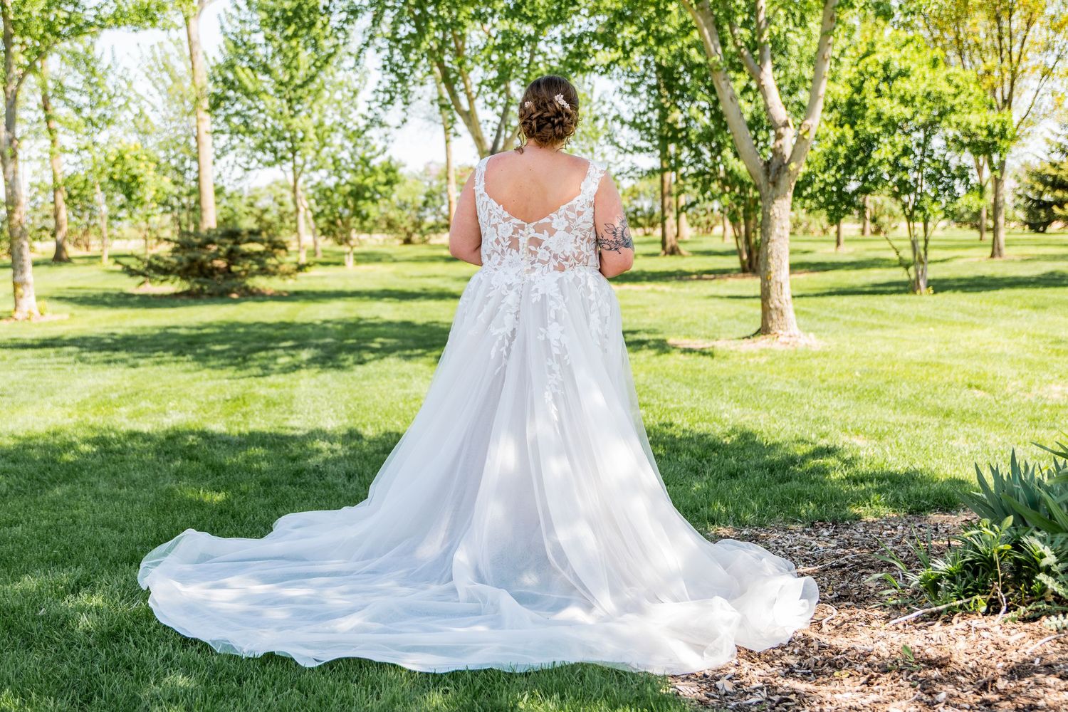 Back view of lace wedding dress with flowing train against green garden background.