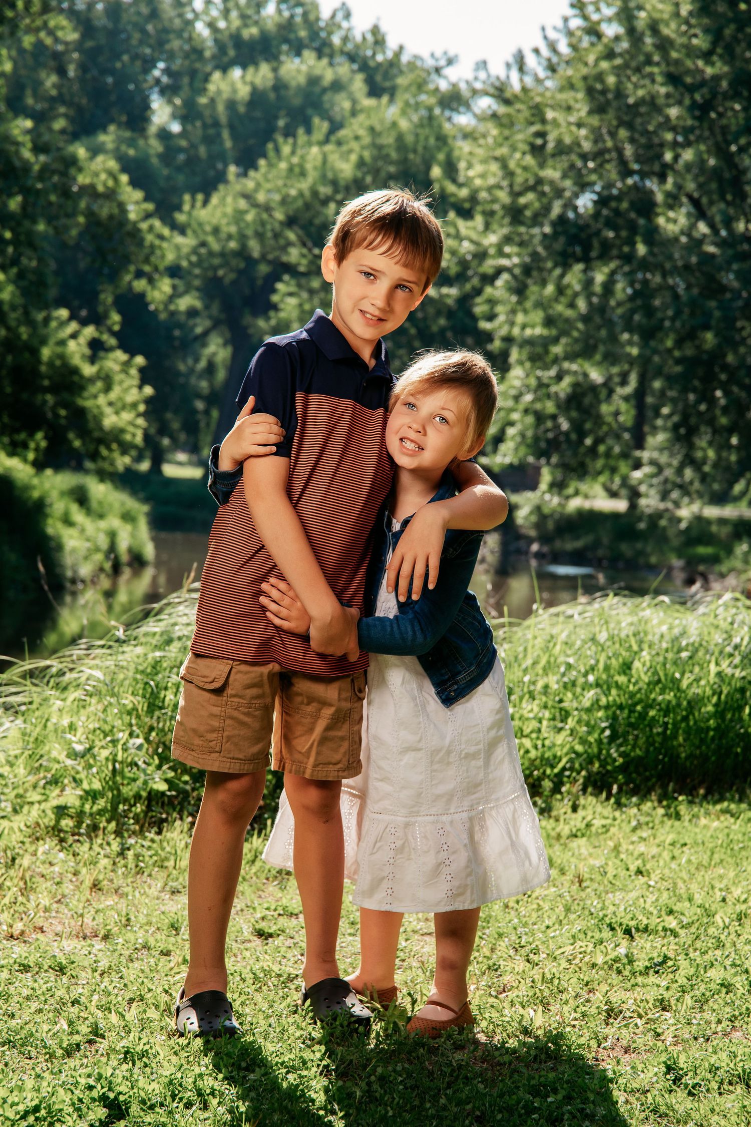 Two children playing together in a sunny green field with trees in the background on a summer day.