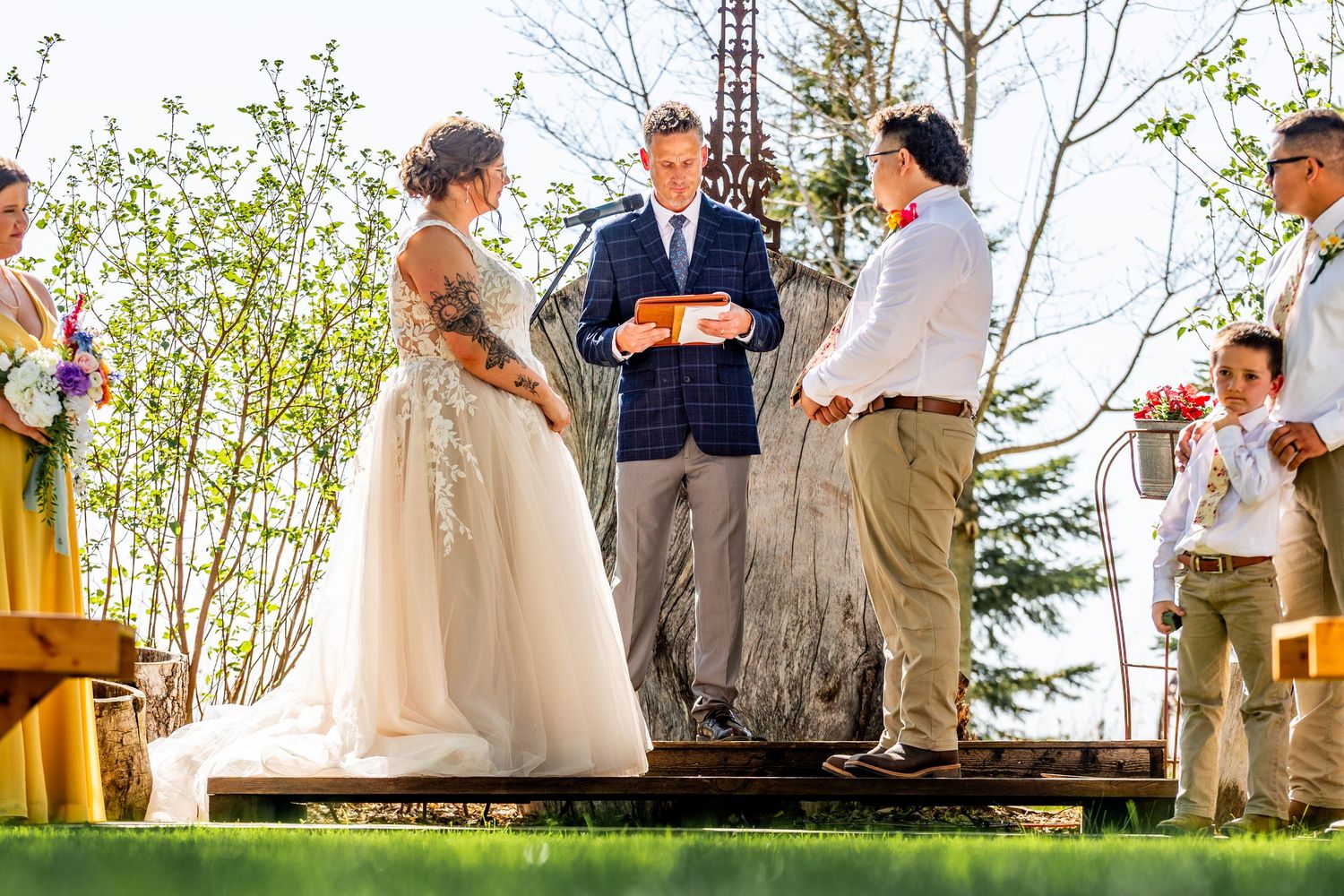 Outdoor wedding ceremony on wooden platform surrounded by spring foliage.