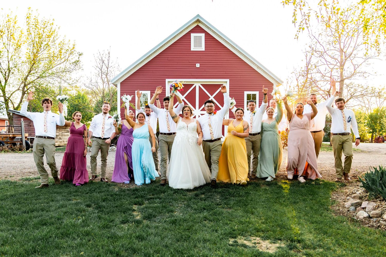 Wedding group photo with bright colorful dresses against a red barn backdrop.