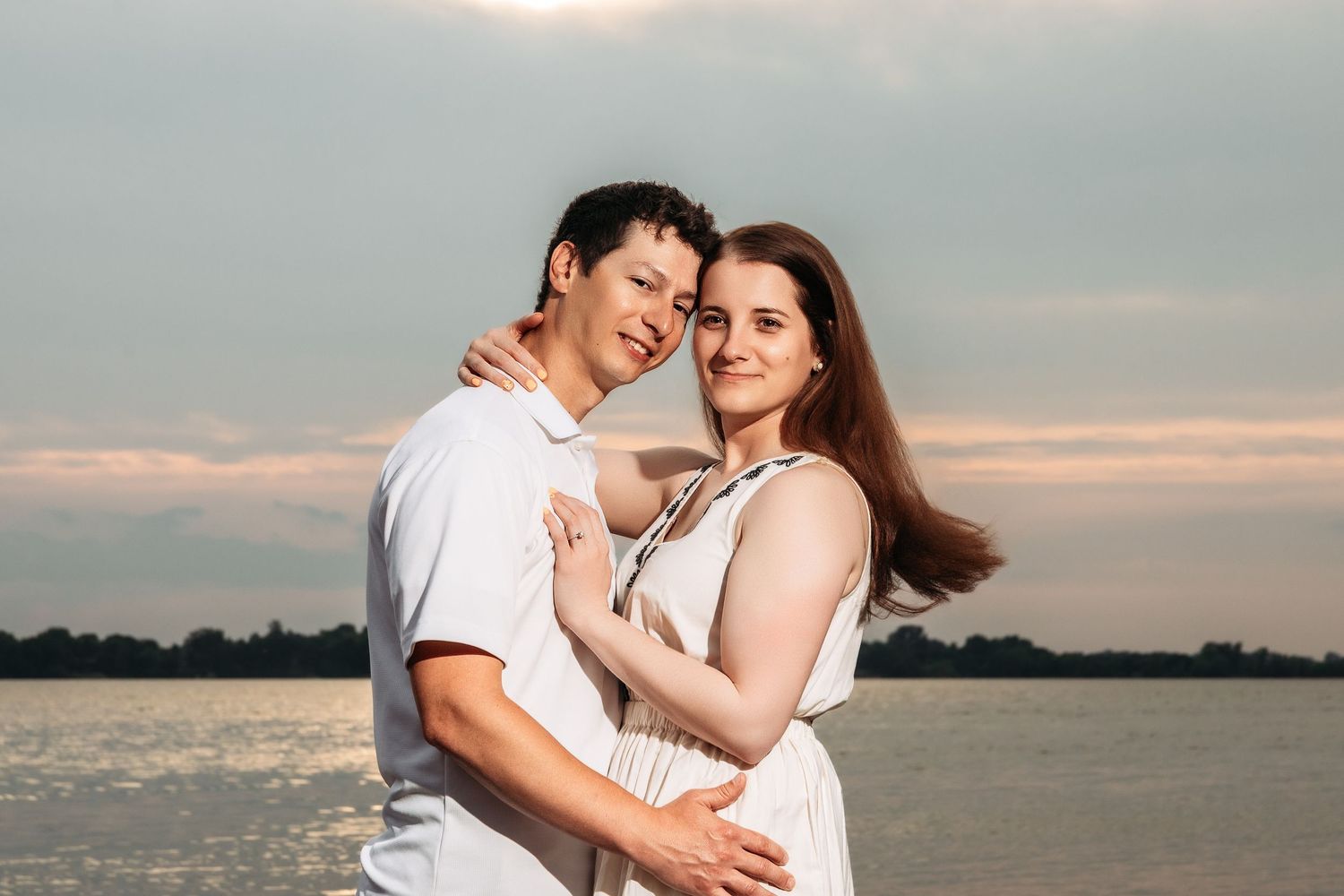 Affectionate couple shares intimate moment at sunset by waterfront.