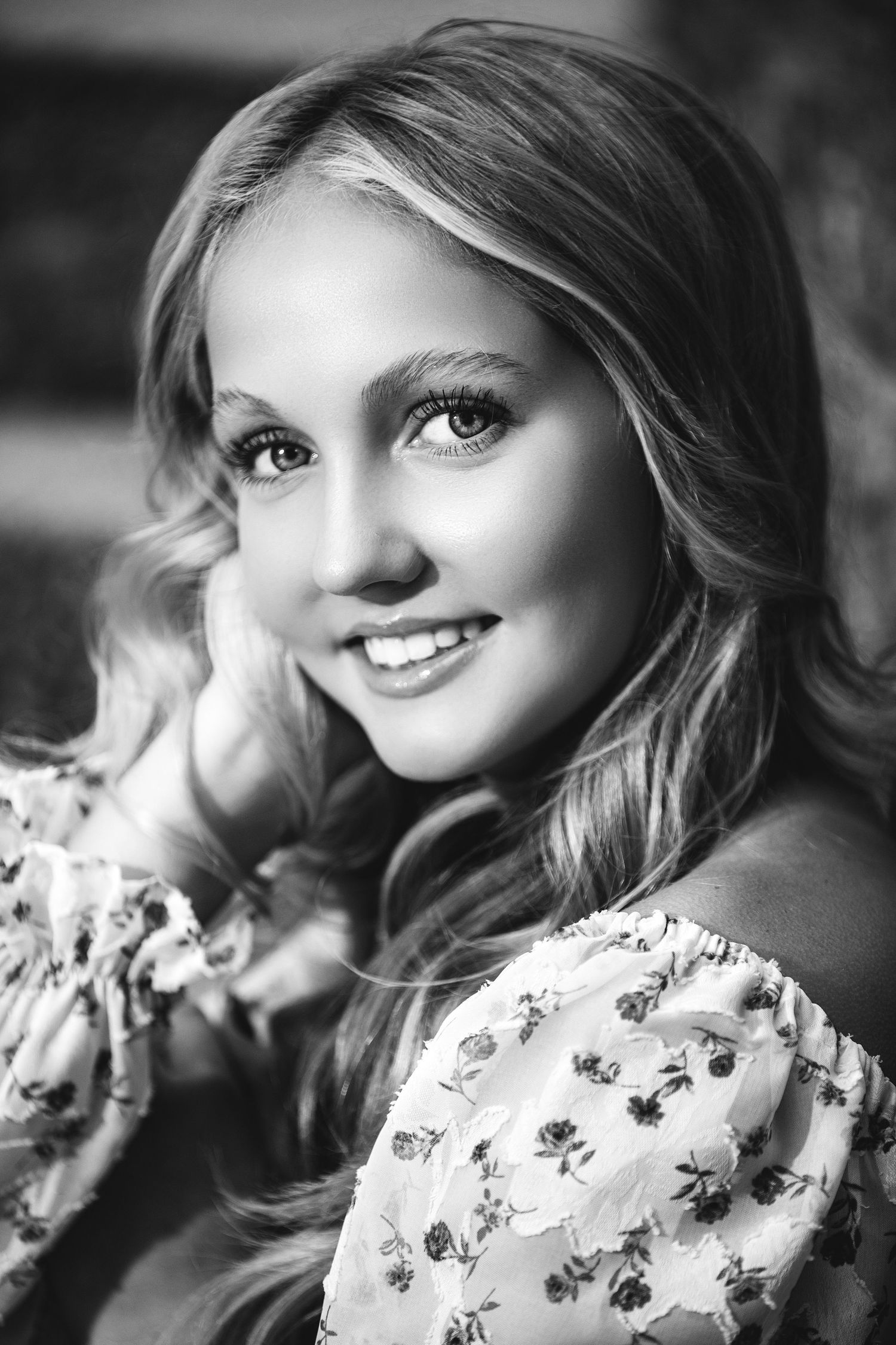 Portrait of a young person in a floral dress smiling against a dark background in black and white.