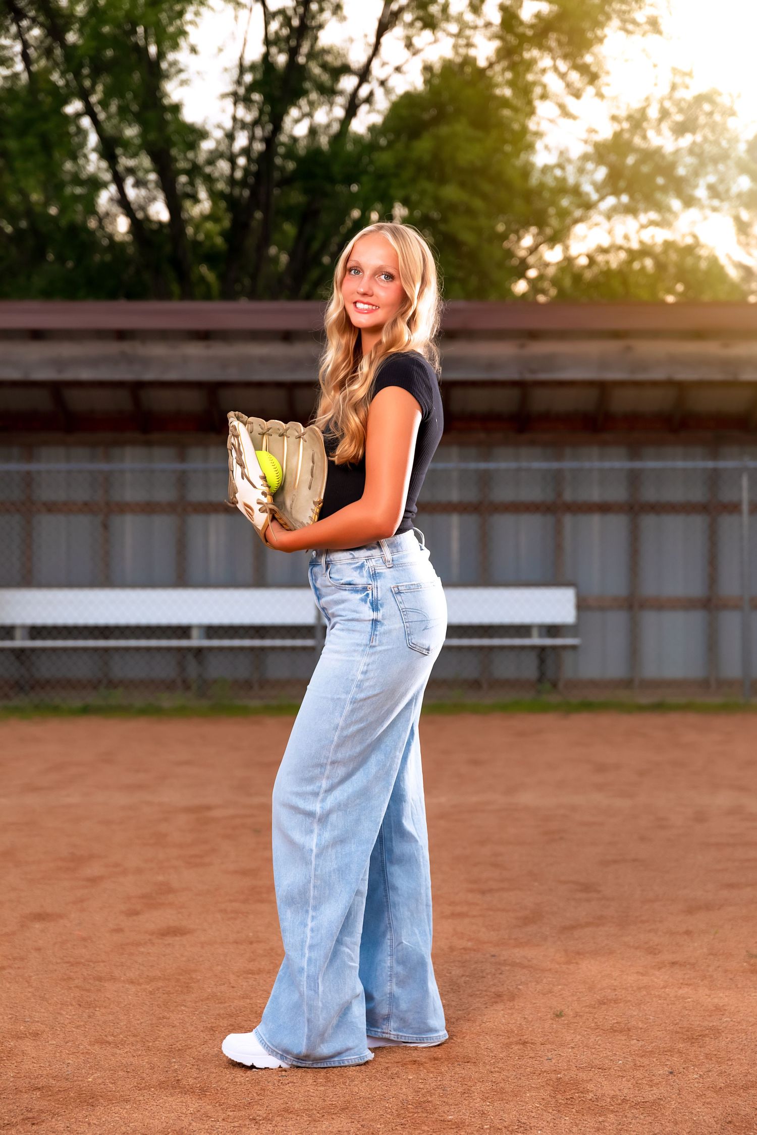 Outdoor senior portrait session with athletic theme on baseball diamond at golden hour.