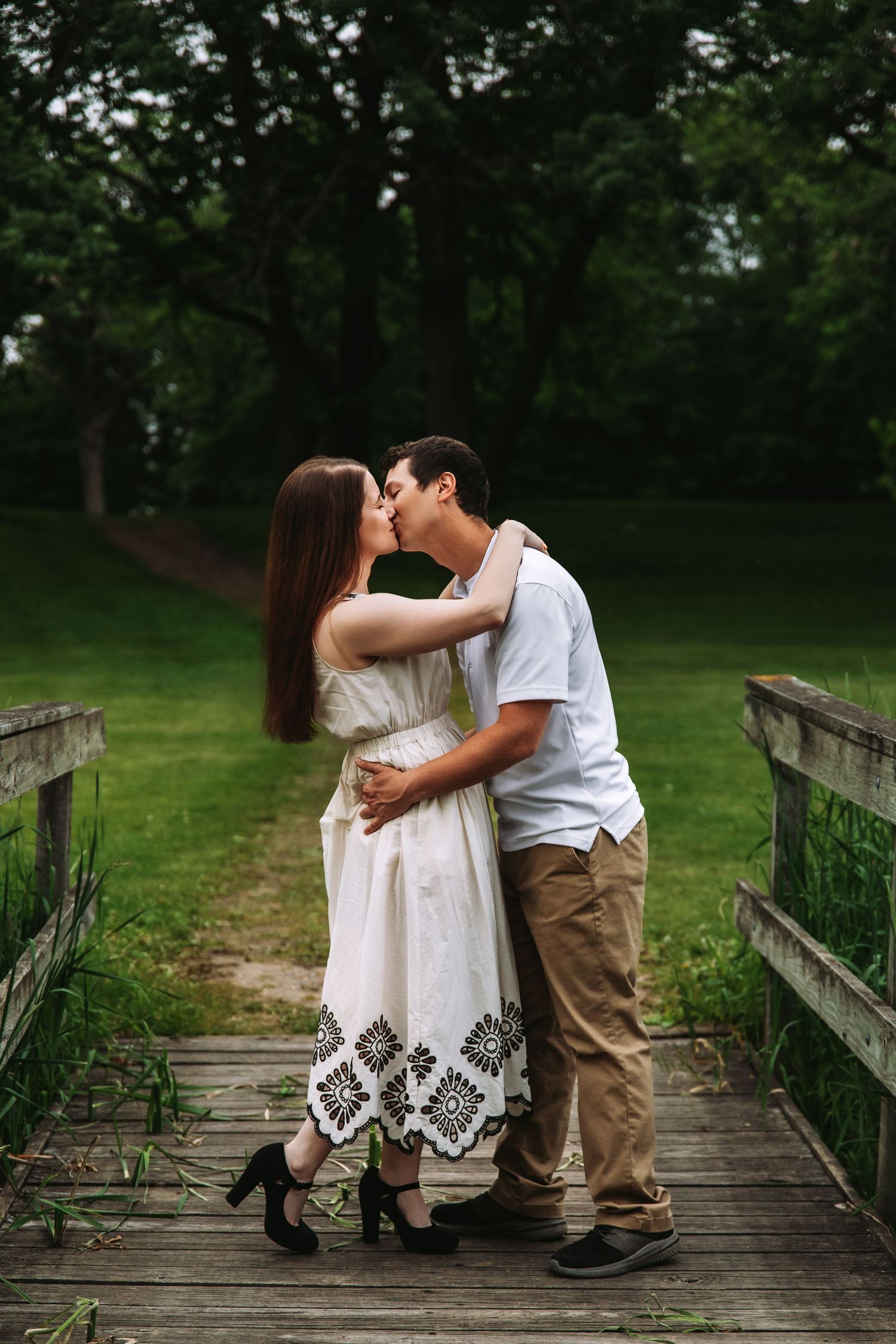 A couple sits close together on a rustic wooden boardwalk surrounded by lush green scenery.