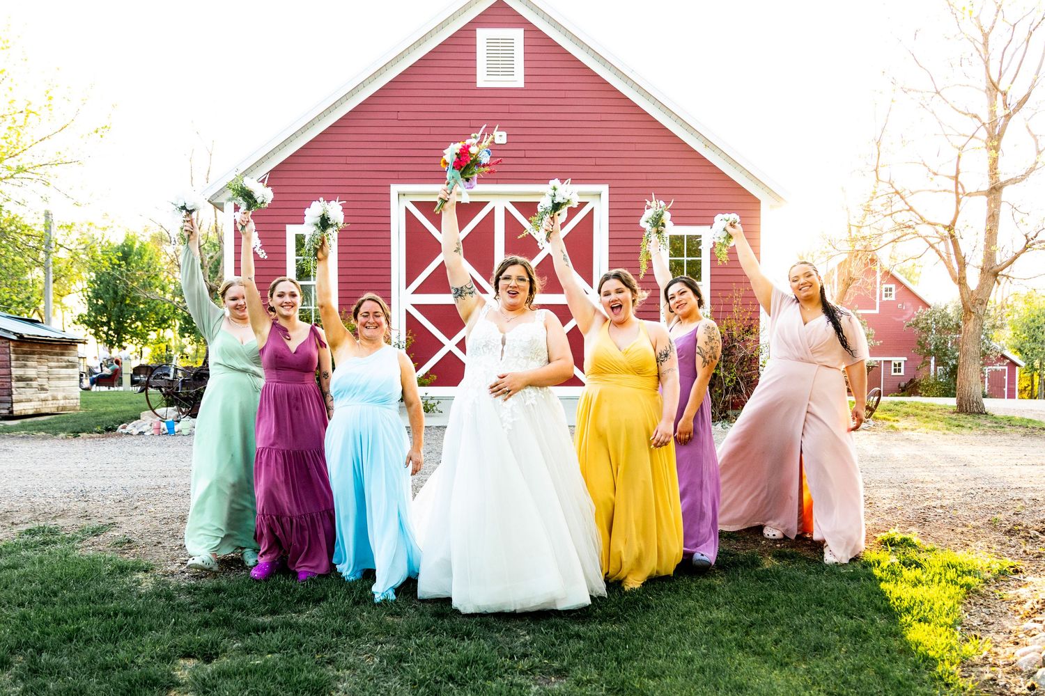 Wedding party group photo in pastel dresses lined up against a classic red barn backdrop.