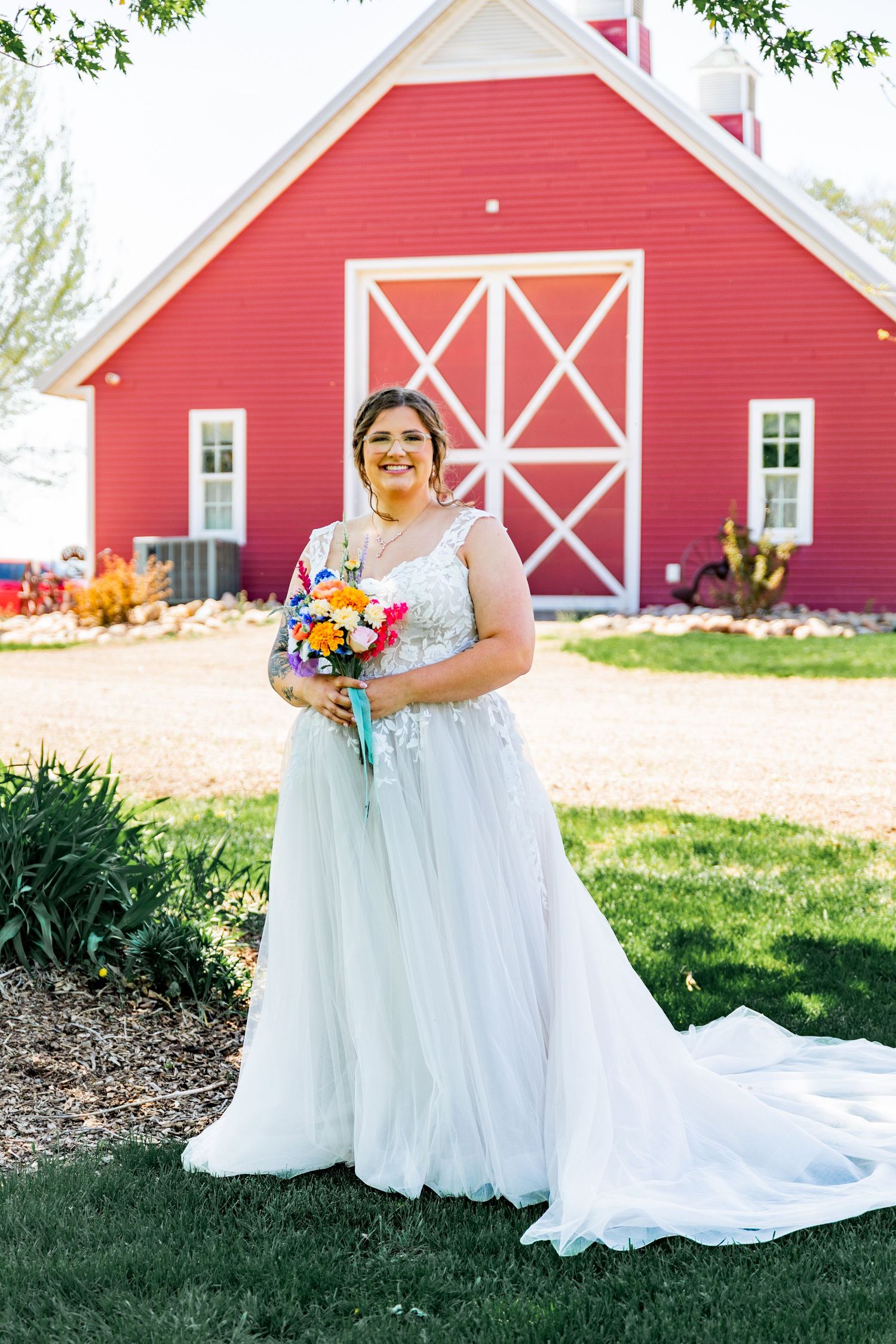 Wedding photos in front of a red barn featuring a white wedding dress against rustic farmhouse architecture.