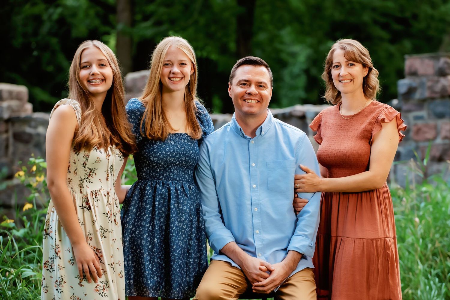 A family in coordinated blue and rust-colored outfits sits together outdoors for portraits in a natural setting in Southwest Minnesota.