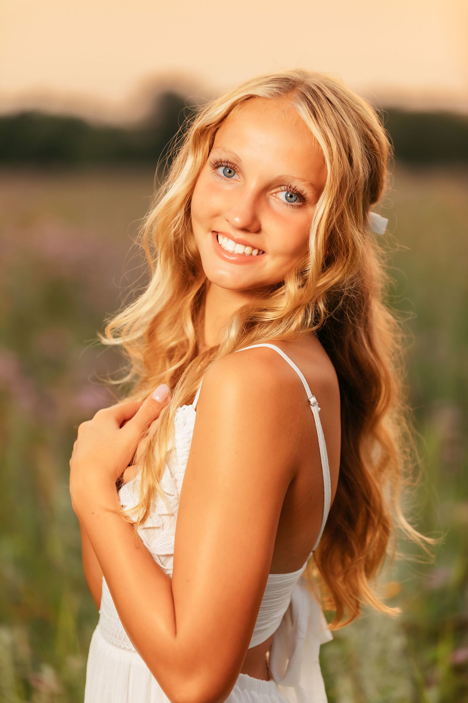 Golden hour portrait in a meadow featuring soft lighting and a white sundress among summer wildflowers.