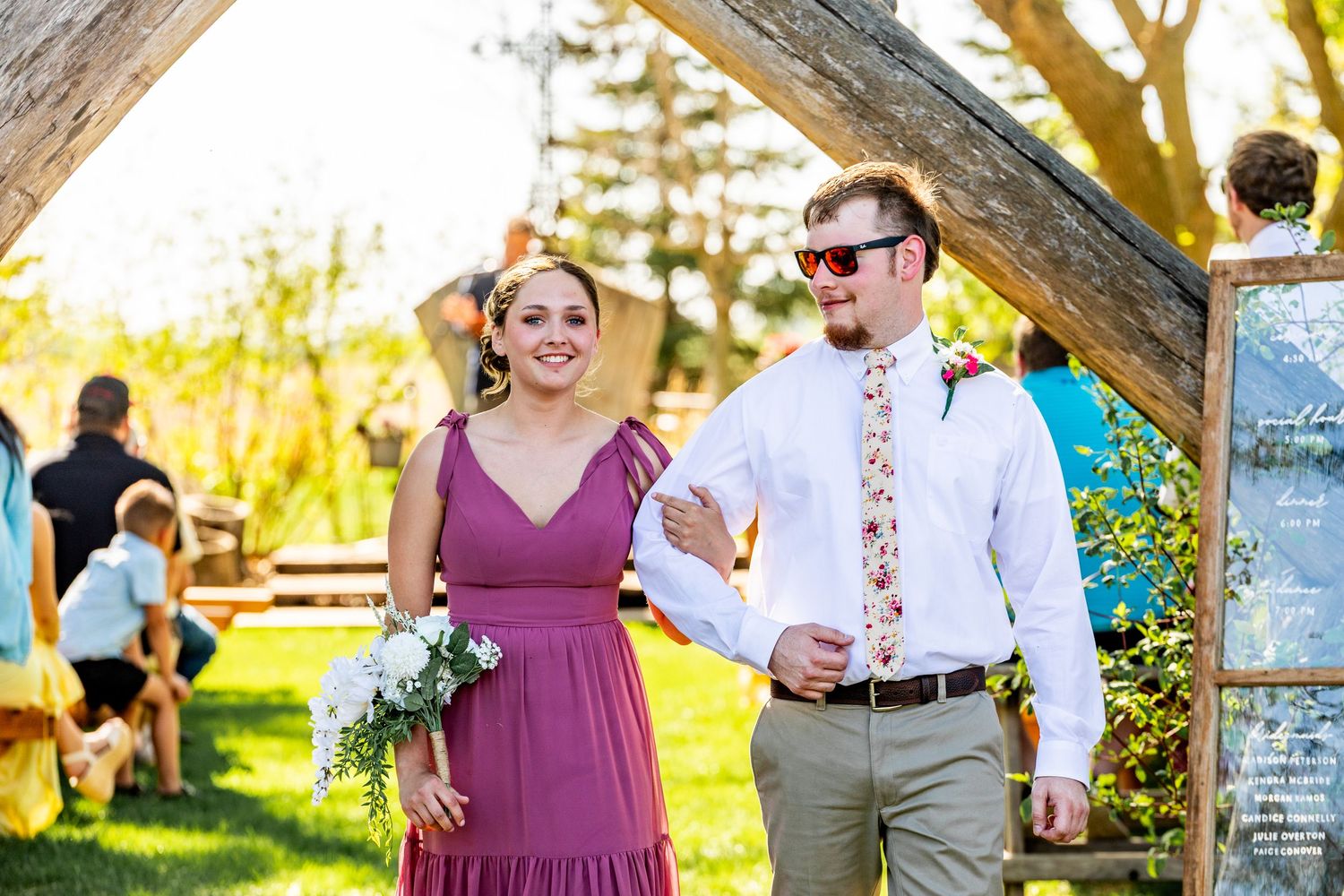Wedding guests gather under trees in a scenic outdoor setting during golden hour.