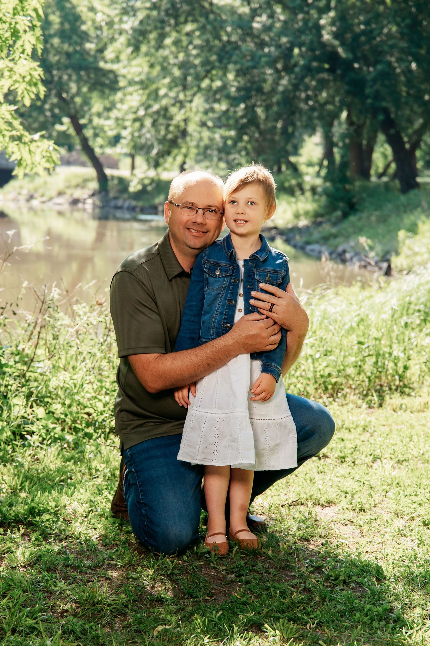 Two people sitting together on grassy slope near pond sharing a tender moment outdoors.